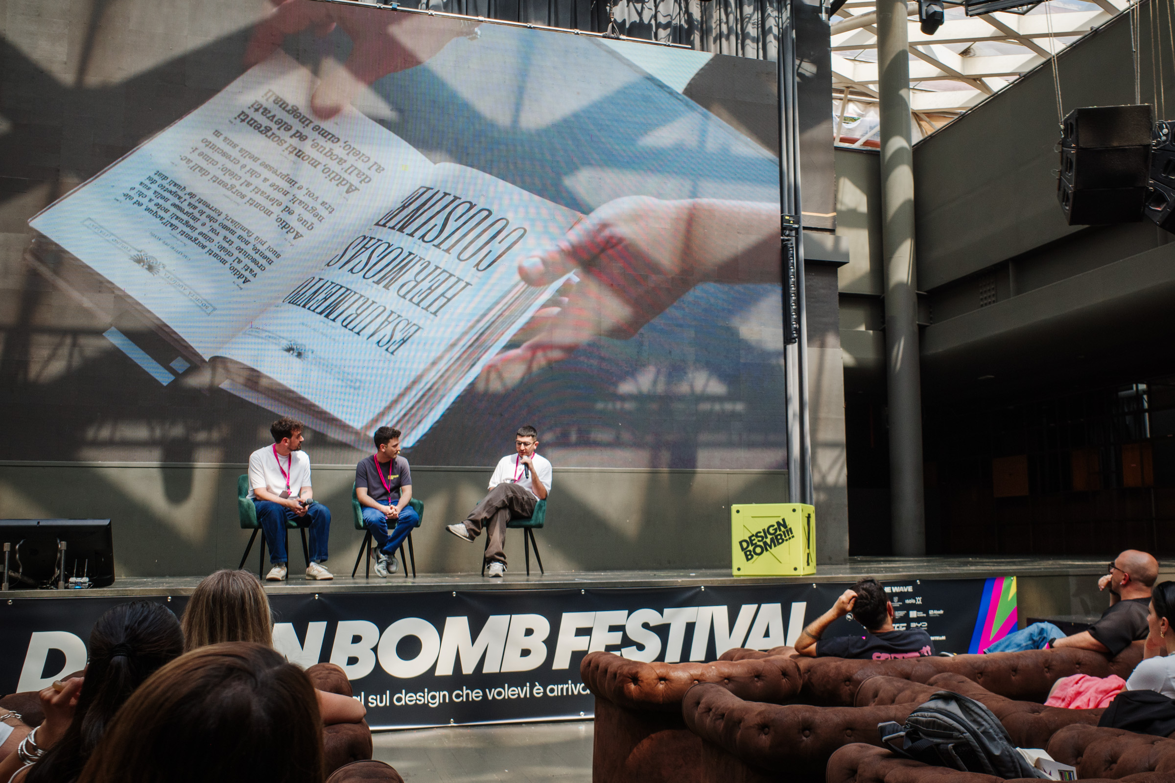 PierCarlo Tozzi intervistato sul palco del Design Bomb Festival con uno schermo che mostra un libro aperto