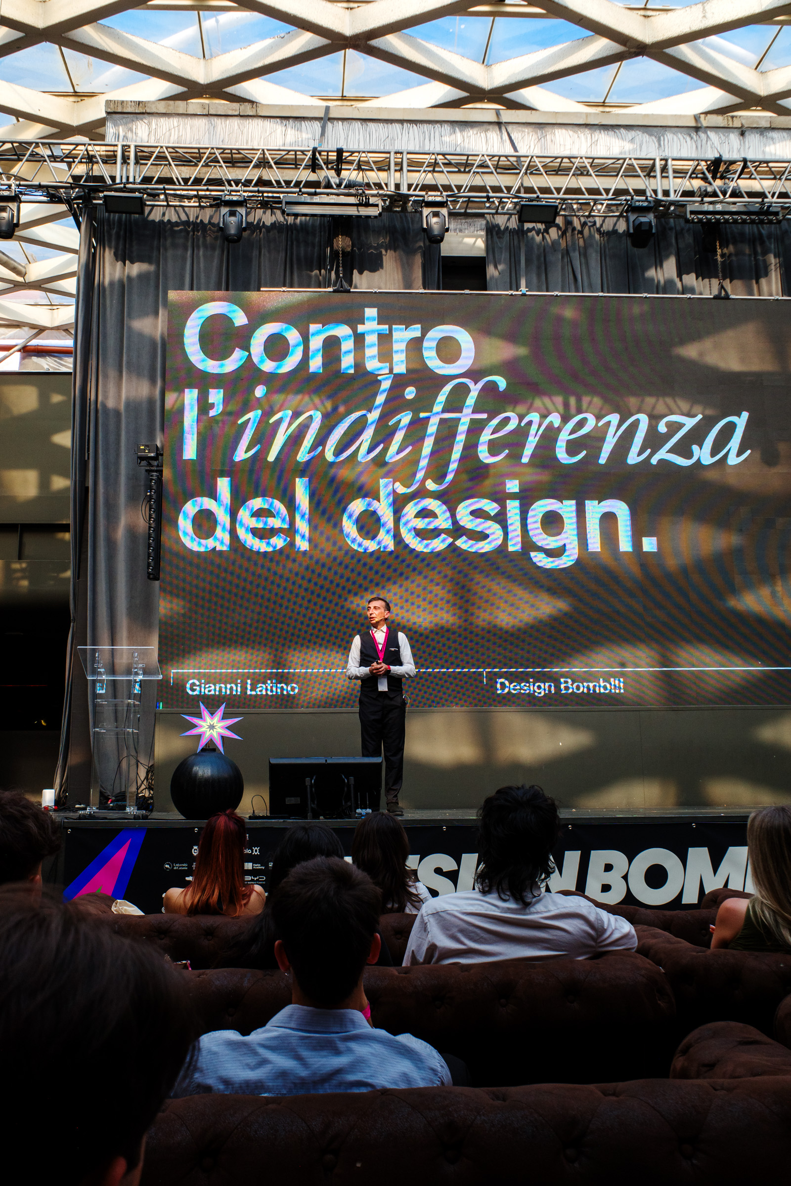 Gianni Latino sul palco con lo schermo che mostra la slide Contro l'indifferenza del design